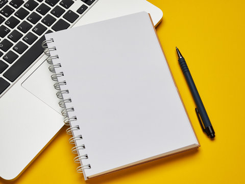 Workplace - laptop, notebook and pen for remote work on a yellow background table. Freelance desktop for home or office. Background with copy space. - Powered by Adobe