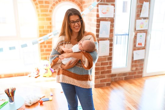 Young beautiful woman and her baby standing at home. Mother holding and hugging newborn