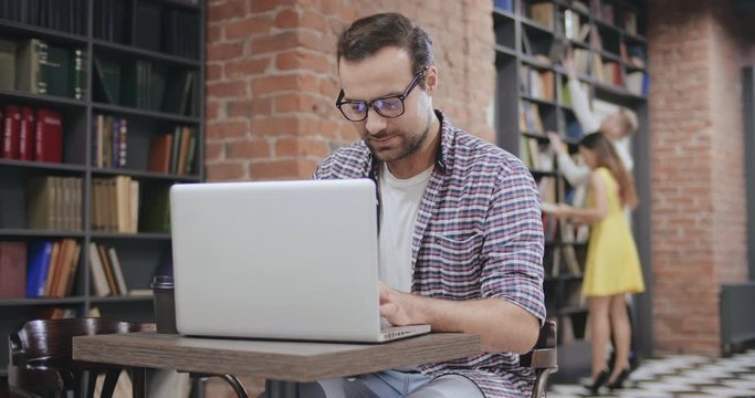Handsome young man using laptop sitting in library