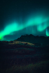 Image of Northern Lights illuminating the sky with a mountain landscape backdrop in Iceland during night time 