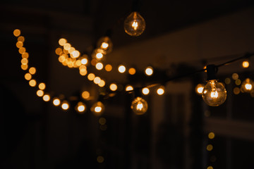 Luminous incandescent lamps hang in the form of a garland on wires, against the background of a...