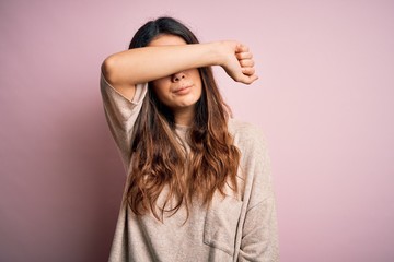 Fototapeta premium Young beautiful brunette woman wearing casual sweater standing over pink background covering eyes with arm, looking serious and sad. Sightless, hiding and rejection concept