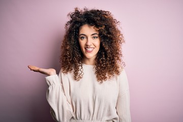 Beautiful woman with curly hair and piercing wearing casual sweater over pink background smiling...