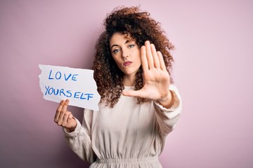 Young beautiful woman with curly hair and piercing holding paper with love yourself message with...