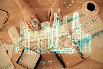 Double exposure of man's hands typing over computer keyboard and buildings drawing. Top view. smart city concept.