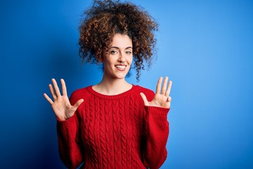 Young beautiful woman with curly hair and piercing wearing casual red sweater showing and pointing up with fingers number nine while smiling confident and happy.