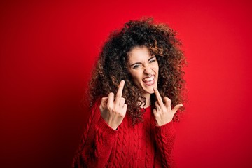 Young beautiful woman with curly hair and piercing wearing casual red sweater Showing middle finger...