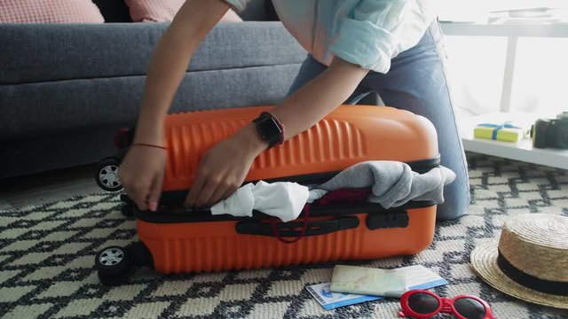 Cute girl standing on her knees on overfilled orange suitcase, trying to close it