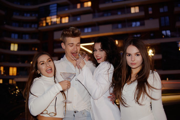 Girls, girlfriends having fun near the golden car. Girls all in white with a man, friendship. Girls celebrate. Girlfriends have fun and drink alcohol in glasses. 