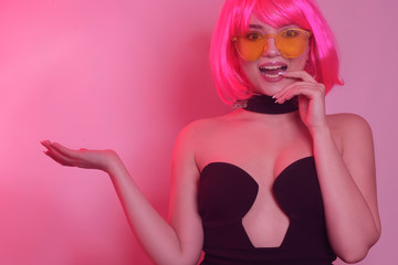 A bright girl on a pink background, in a pink short wig with a bang, holds her hand. A girl advertises your product, free space for text. Anchor photo to advertise your product. Girl shows