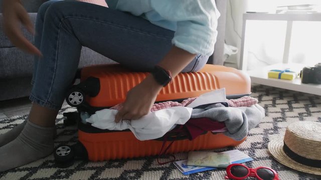 Cute girl sitting on a overfilled suitcase, trying to close it