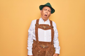 Senior grey-haired man wearing german traditional octoberfest suit over yellow background In shock...