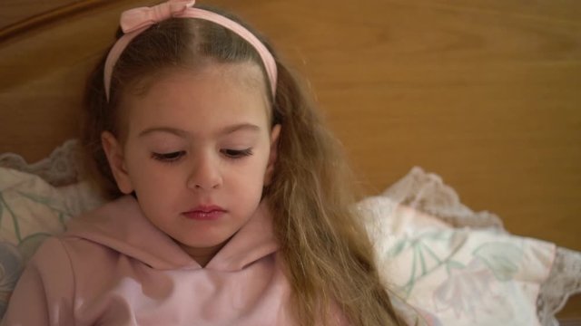 Girl shows tongue. Naughty child in bed not wanting sleep.