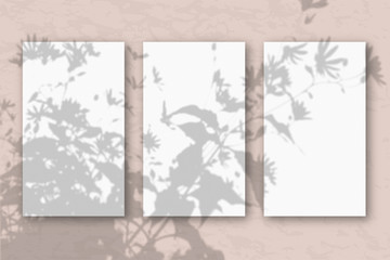 3 vertical sheets of white textured paper on a pastel pink wall background. Mockup with an overlay of plant shadows. Natural light casts a shadow from the top of the field plants and flowers