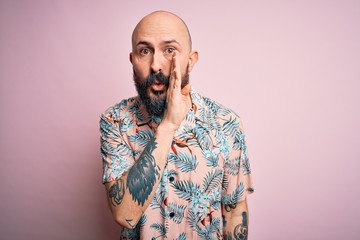 Obraz premium Handsome bald man with beard and tattoo wearing casual floral shirt over pink background hand on mouth telling secret rumor, whispering malicious talk conversation