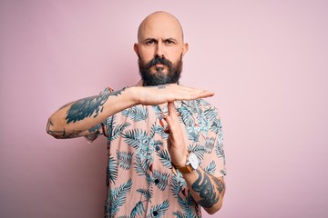 Handsome bald man with beard and tattoo wearing casual floral shirt over pink background Doing time...