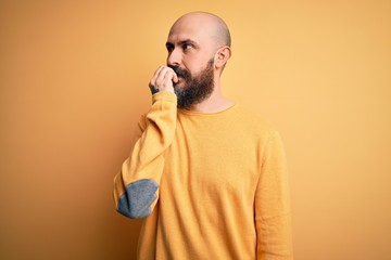 Handsome bald man with beard wearing casual sweater standing over yellow background looking stressed and nervous with hands on mouth biting nails. Anxiety problem.