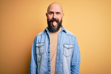 Fototapeta premium Handsome bald man with beard wearing casual denim jacket and striped t-shirt sticking tongue out happy with funny expression. Emotion concept.