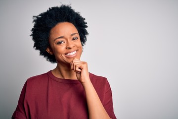 Fototapeta na wymiar Young beautiful African American afro woman with curly hair wearing casual t-shirt standing looking confident at the camera with smile with crossed arms and hand raised on chin. Thinking positive.