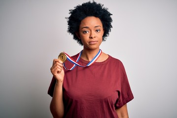 Young African American athlete woman with curly hair wearing gold medal winner competition with a confident expression on smart face thinking serious