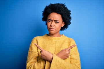 Young beautiful African American afro woman with curly hair wearing yellow casual sweater Pointing to both sides with fingers, different direction disagree