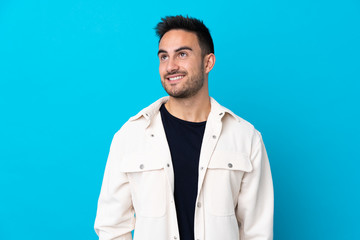 Young handsome man over isolated blue background laughing and looking up