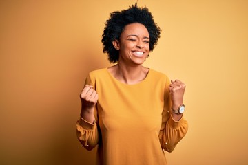 Young beautiful African American afro woman with curly hair wearing casual t-shirt very happy and excited doing winner gesture with arms raised, smiling and screaming for success. Celebration concept.