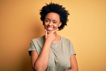 Fototapeta na wymiar Young beautiful African American afro woman with curly hair wearing casual t-shirt looking confident at the camera smiling with crossed arms and hand raised on chin. Thinking positive.