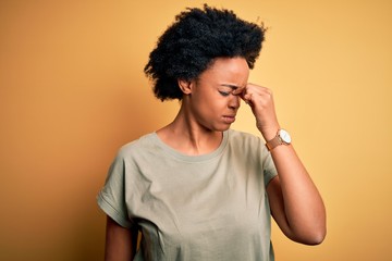 Young beautiful African American afro woman with curly hair wearing casual t-shirt tired rubbing nose and eyes feeling fatigue and headache. Stress and frustration concept.