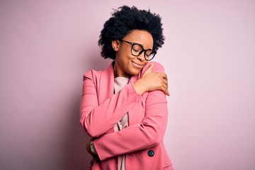 Fototapeta na wymiar Young beautiful African American afro businesswoman with curly hair wearing pink jacket Hugging oneself happy and positive, smiling confident. Self love and self care