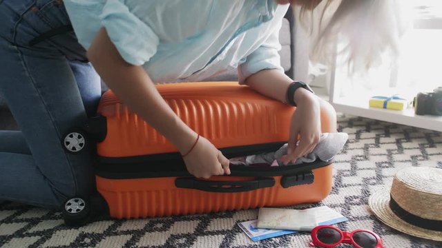 Young girl standing on elbowson on overfilled orange suitcase, trying to close it