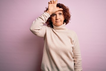 Middle age beautiful curly hair woman wearing casual turtleneck sweater over pink background making...