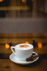 A mug of hot cappuccino with cinnamon on a saucer stands on a wooden table in a cafe.