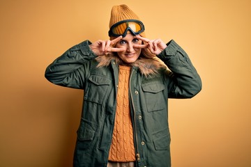 Middle age beautiful blonde skier woman wearing snow sportwear and ski goggles Doing peace symbol with fingers over face, smiling cheerful showing victory