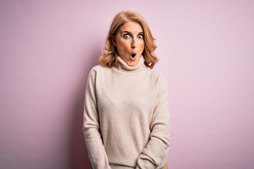 Middle age beautiful blonde woman wearing casual turtleneck sweater over pink background afraid and...