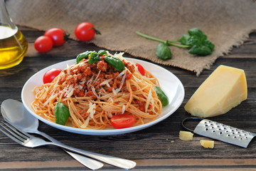 Spaghetti Bolognese with fresh tomatoes, basil and parmesan cheese on a rustic wooden dark table.