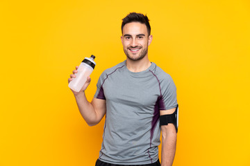 Sport man over isolated yellow wall with sports water bottle