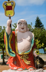 A smiling Buddha statue holding an upside down tile guitar welcomes visitors the the shrine at Repulse Beach Hong Kong.