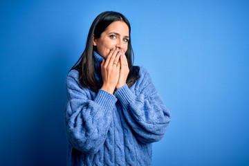 Young brunette woman with blue eyes wearing casual turtleneck sweater laughing and embarrassed giggle covering mouth with hands, gossip and scandal concept