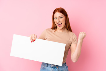 Young redhead woman over isolated pink background holding an empty white placard for insert a concept
