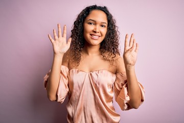 Young beautiful woman with curly hair wearing casual t-shirt standing over pink background showing...
