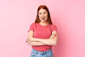 Young redhead woman over isolated pink background working with headset