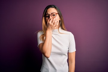 Young beautiful blonde woman with blue eyes wearing casual t-shirt over purple background smelling...