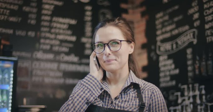 Female smiling bar tender talking on phone in coffee shop
