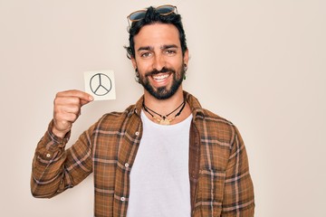 Fototapeta premium Young handsome hispanic bohemian hipster man with bear holding paper note with peace symbol with a happy face standing and smiling with a confident smile showing teeth