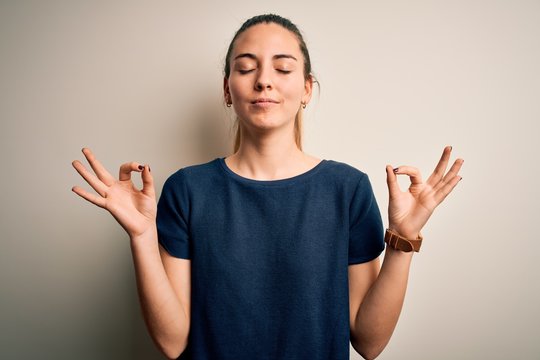 Young beautiful blonde woman with blue eyes wearing casual t-shirt over white background relax and smiling with eyes closed doing meditation gesture with fingers. Yoga concept.
