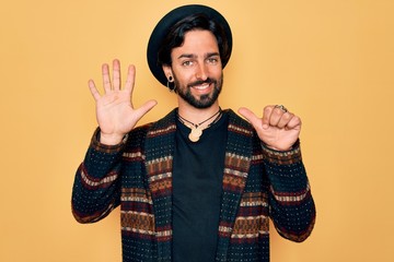 Young handsome hispanic bohemian man wearing hippie style and boho hat showing and pointing up with...