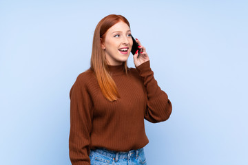 Young redhead woman over isolated blue background keeping a conversation with the mobile phone