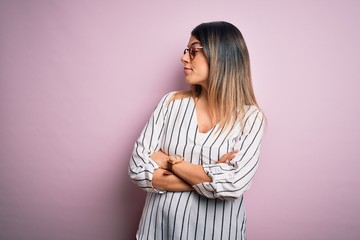 Fototapeta premium Young beautiful woman wearing casual striped t-shirt and glasses over pink background looking to the side with arms crossed convinced and confident