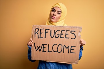 Beautiful arab woman wearing islamic hijab holding banner with refugees welcome message with a...